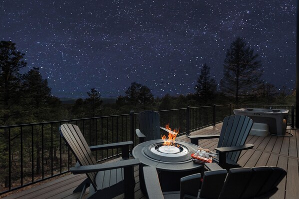 Une terrasse dotée de chaises Adirondack, d’un foyer et d’un jacuzzi, le tout sous un ciel étoilé.