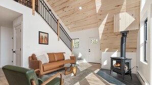 A modern living room with a staircase, a fireplace, and a green chair. - Brand New A-Frame! Panoramic Mt Views, Hot Tub, Speakeasy, EV Charger (Florissant)