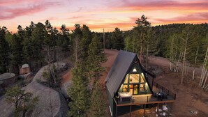 A cabin with a deck, surrounded by trees and rocks. - Brand New A-Frame! Panoramic Mt Views, Hot Tub, Speakeasy, EV Charger (Florissant)