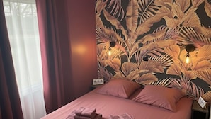 Ein Bett mit Kopfteil in Blattformmuster, zwei Nachttischlampen und ein ordentlich bezogenes Bett mit gefalteten Handtüchern.