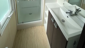 Ein Badezimmer mit einer Duschkabine aus Glas, einem weißen Waschbecken mit Spiegel und Holzschränken.
