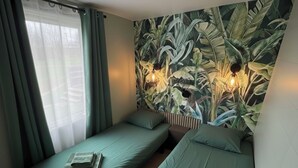 Ein Zimmer mit zwei Einzelbetten, einem Fenster mit durchsichtigen Vorhängen und einer Wandmalerei mit tropischen Blättern.