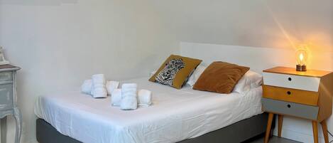 A neatly made bed with white linens, a bedside table with a lamp, and a wall-mounted air conditioner.