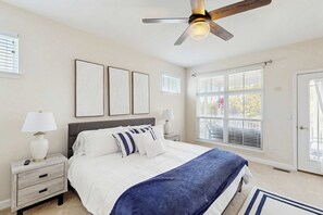 Ein Schlafzimmer mit einem Bett, Nachttischen, einem Deckenventilator und großen Fenstern.