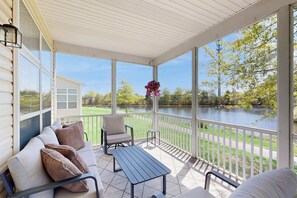 Eine überdachte Veranda mit Seeblick, eine weiße Couch mit Kissen, ein Tisch und ein Stuhl.