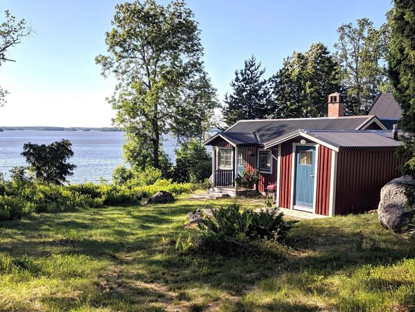 A cabin by a lake with a clear view of the water, surrounded by trees and greenery.