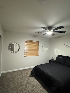 A bedroom with a bed, a ceiling fan, a wall clock, and a window with blinds.