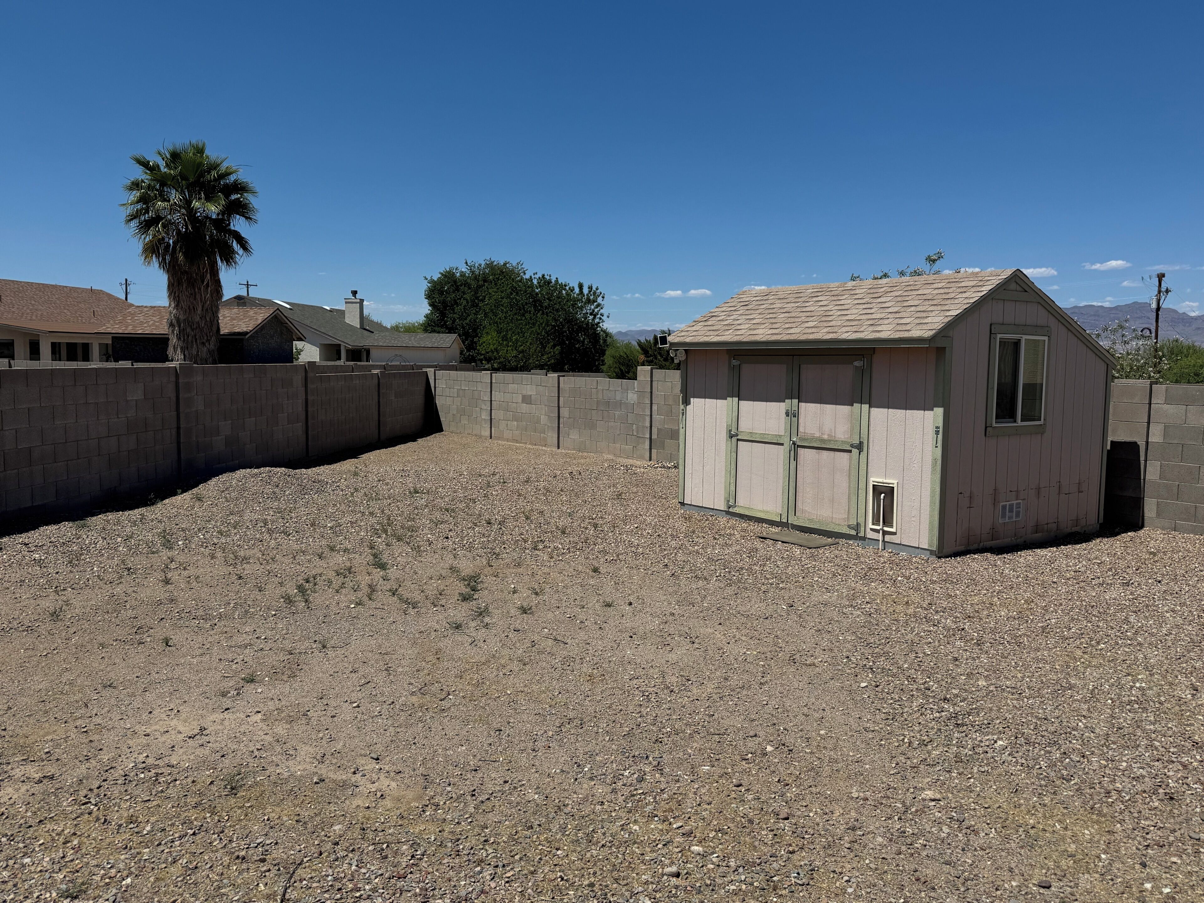 A small shed with a sloped roof and a window, surrounded by a gravel area and a concrete wall.