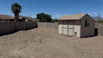 A small shed with a sloped roof and a window, surrounded by a gravel area and a concrete wall.