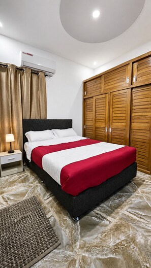 A bedroom with a bed, a nightstand, an air conditioning unit, and wooden wardrobes.