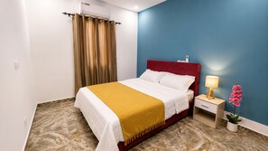 A hotel room with a bed, a nightstand, a lamp, and a potted plant.