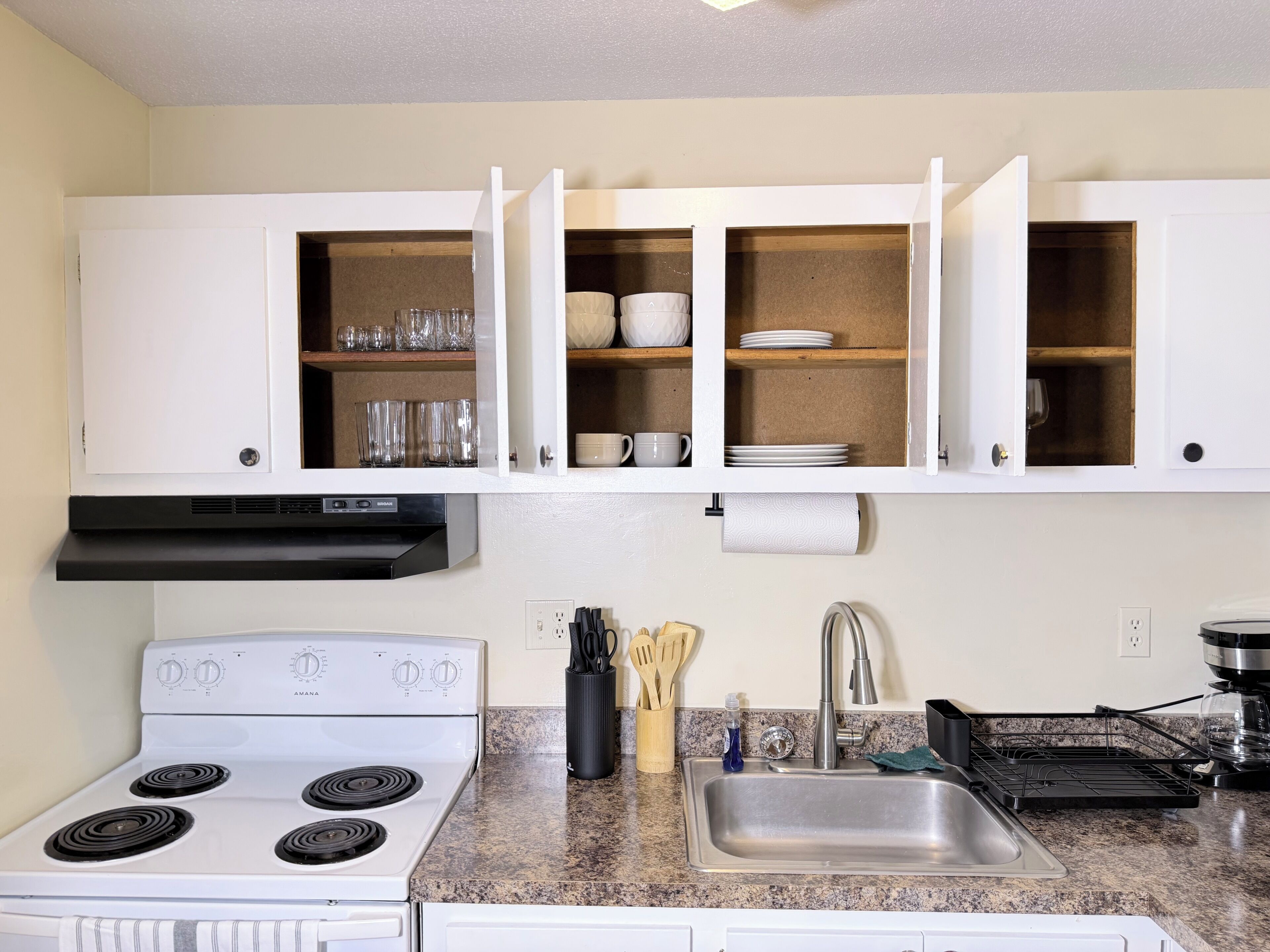 A kitchen with white cabinets, a stove, a sink, and various utensils.