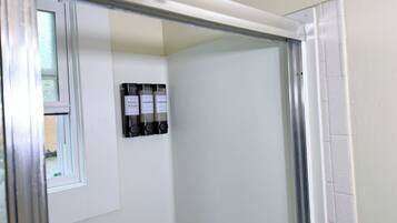 A bathroom with a shower, a window, and three bottles of shampoo and conditioner on the wall.