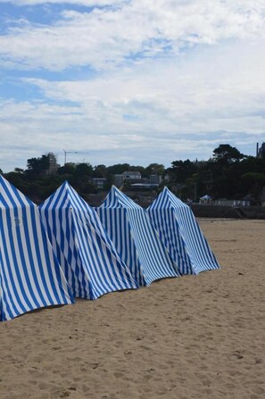 A row of striped beach tents on a sandy beach with a cloudy sky and buildings in the background. - Ker Helios - DINARD - City break (DINARD)