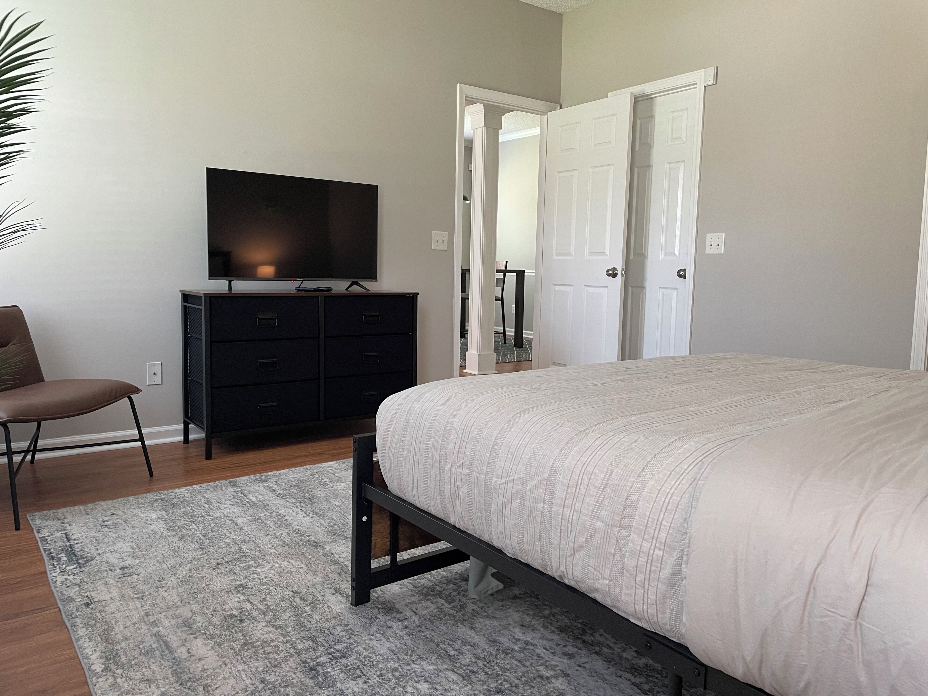 Un dormitorio con una cama, un televisor sobre un aparador, una silla y una puerta.