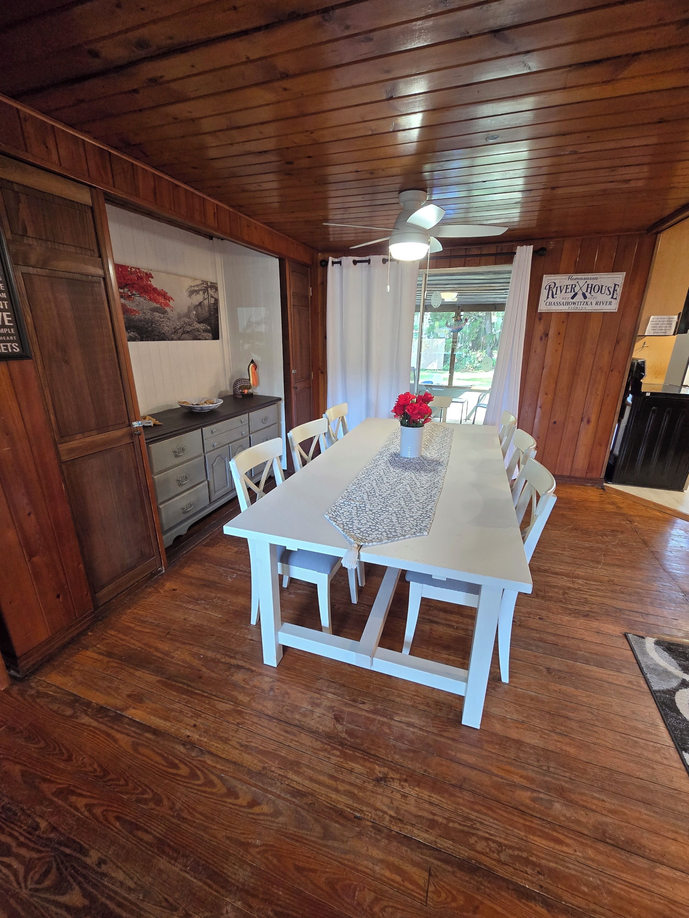 A wooden dining room with a white table, chairs, and a ceiling fan.