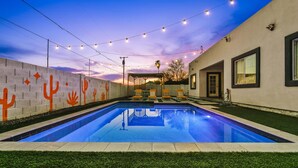 Ein Schwimmbecken mit Sonnenuntergangsblick, Lichterketten und einer Wand mit Kaktus-Motiven.