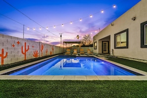 Ein Schwimmbecken mit Sonnenuntergangsblick, Lichterketten und einer Wand mit Kaktus-Motiven.