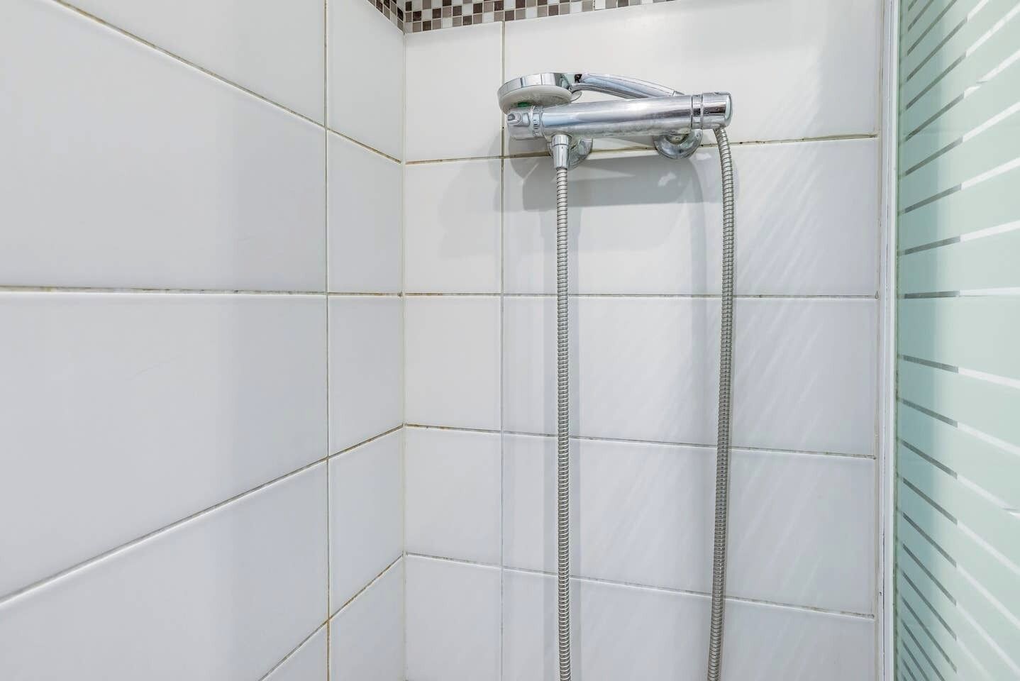 Une douche dotée d’un robinet chromé et d’un flexible, installée dans une salle de bain carrelée à agencement d’angle.