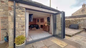 Ein Steinhaus mit Glastür, das in einen Innenraum führt, der eine Couch, einen Tisch und einen Kamin beinhaltet.