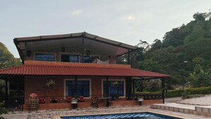 A two-story building with a swimming pool, outdoor seating, and a view of the surrounding greenery. - Villa Veronica large house with beautiful view and spacious for large families  (Sasaima)