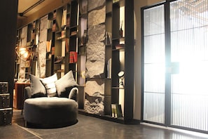 Un salon moderne avec un canapé, des étagères, un mur décoratif en pierre et une grande fenêtre.
