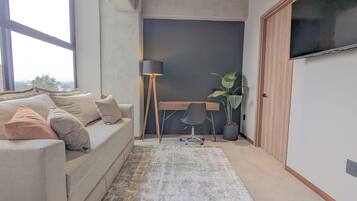 A modern living room with a sofa, a desk, a chair, a floor lamp, and a large window.