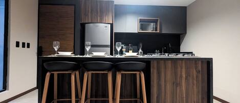 A modern kitchen with a central island, bar stools, a microwave, and a refrigerator.