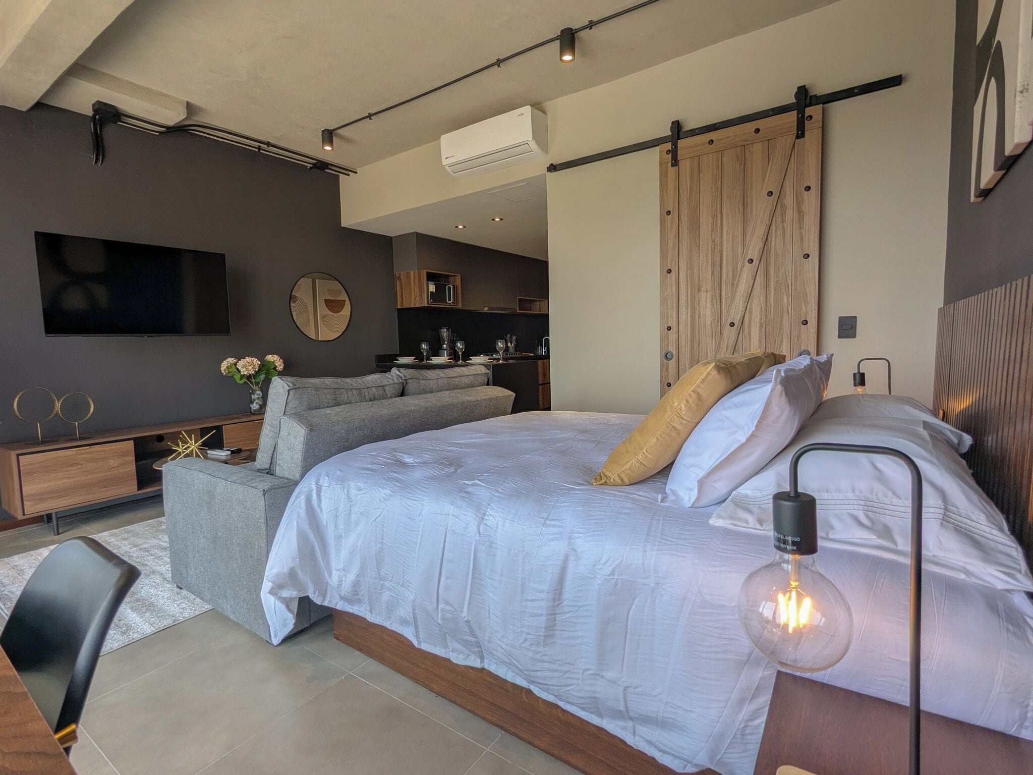 A modern bedroom with a large bed, a TV, a dining area, and a kitchen.