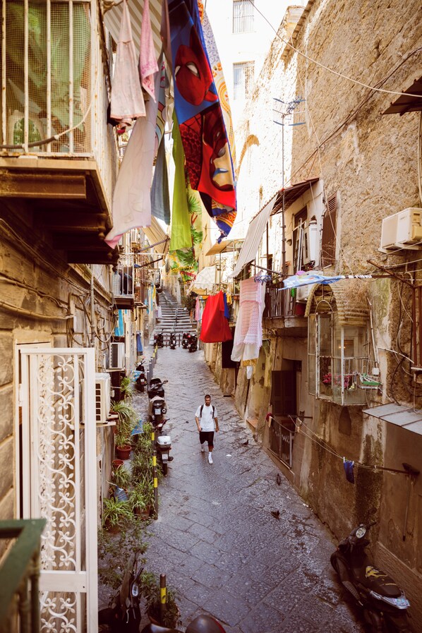 A narrow alley with buildings on either side, a person walking, and hanging laundry. - Tarsia 42 Suites Napoli (Naples)