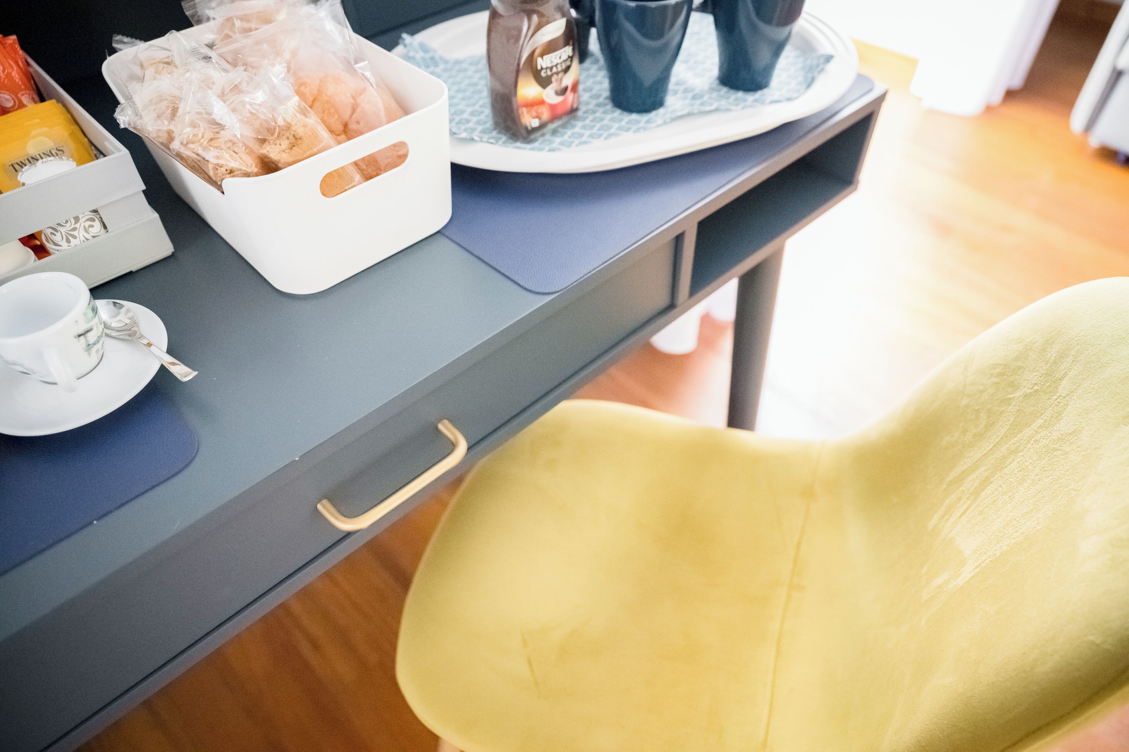 A dining table with a white box of bread, a plate with a bottle, and a cup with a spoon.