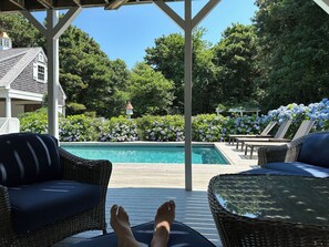 Ett takförsett utomhusområde med en pool, solstolar och en pergola.