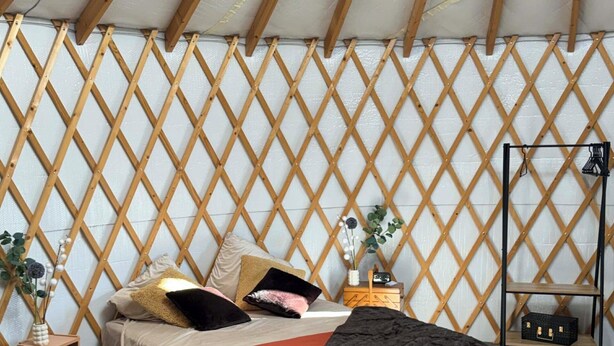 Ein gemütliches Zimmer mit einem Bett, einer Bank, einem kleinen Tisch und einer Wand mit Gittermuster.