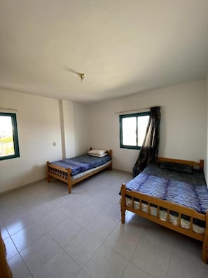 Une chambre avec deux lits en bois, un ventilateur de plafond et deux fenêtres avec des rideaux.