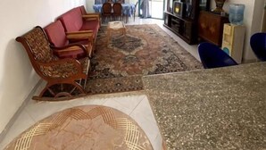 Un saló amb un sofà, cadires, una taula de centre, una televisió i una catifa amb un disseny original.