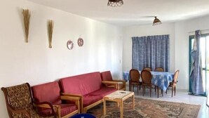 Un saló amb un sofà, cadires, una taula baixa i una zona de menjador amb una taula i cadires.