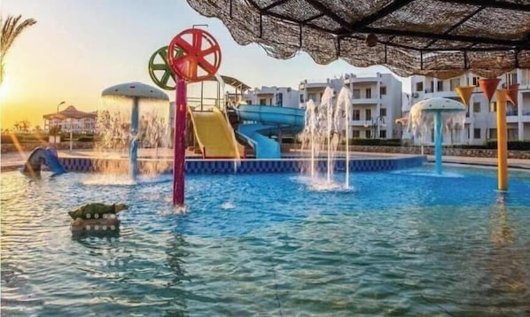 Un parc aquatique doté d’un toboggan aquatique central, de plusieurs fontaines et d’une piscine.