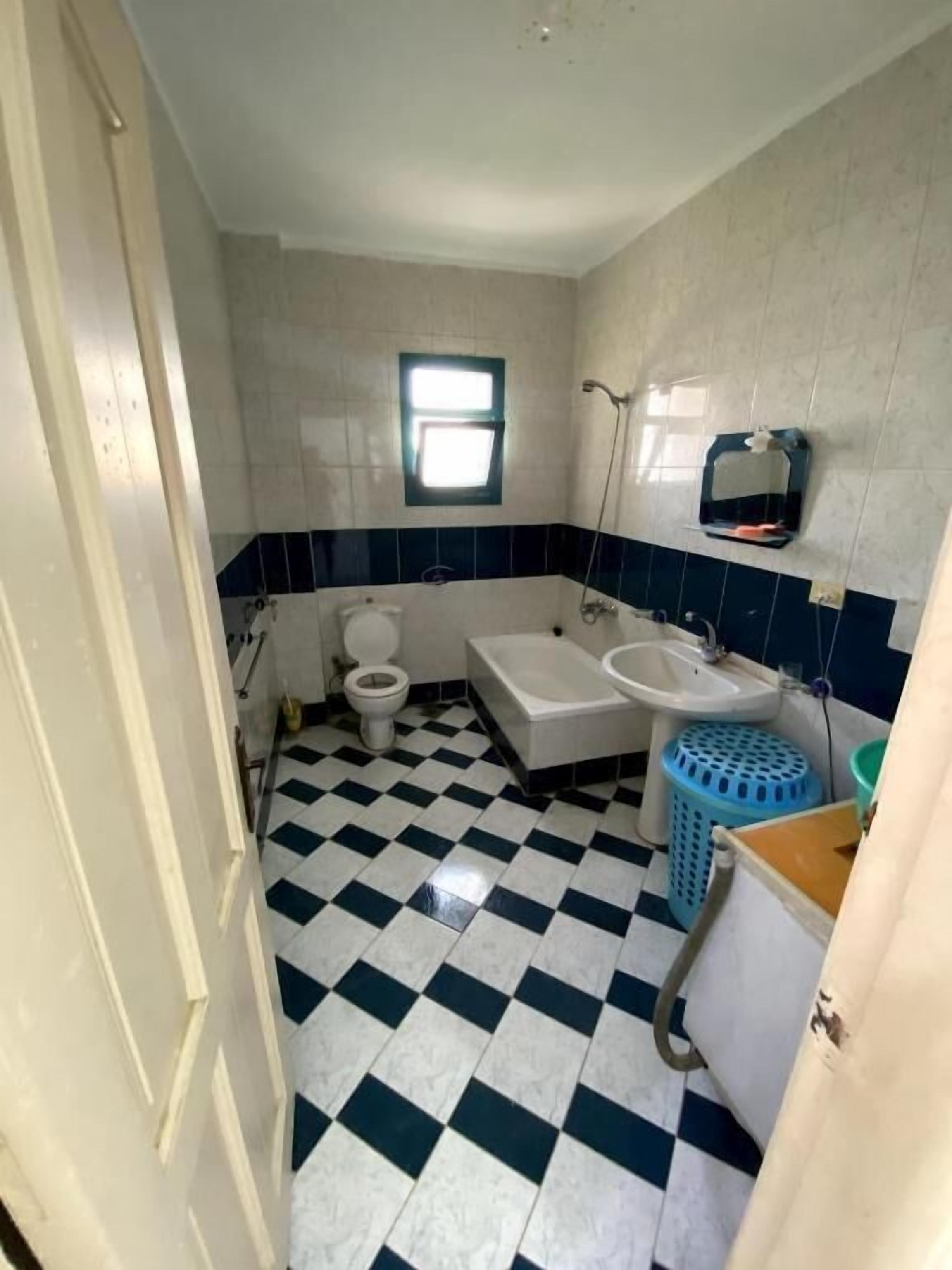 Ein Badezimmer mit Schachbrettboden, Toilette, Badewanne und Waschbecken.
