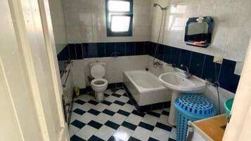 Ein Badezimmer mit Schachbrettboden, Toilette, Badewanne und Waschbecken.