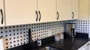 Une cuisine avec des meubles blancs, des poignées noires, un plan de travail noir, un évier en acier inoxydable et un pare-feu décoratif.