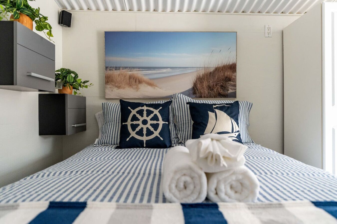 A neatly made bed with striped bedding, a nautical-themed pillow, and a rolled towel.