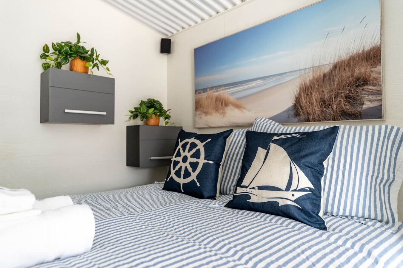 Una cama con ropa de cama a rayas, una almohada con forma de velero y un cuadro con temática náutica.