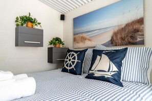 A bed with striped bedding, a sailboat pillow, and a nautical-themed wall art.