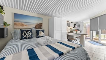 Une chambre à coucher avec un lit, des oreillers, un tableau, un bureau et une vue sur l’extérieur.
