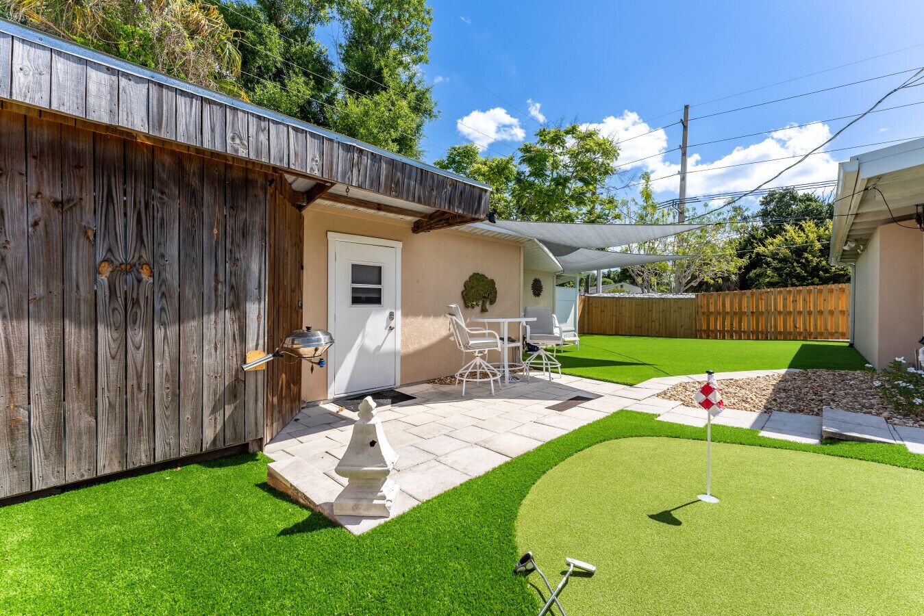 Un jardin avec une terrasse, une pelouse artificielle, un barbecue et du mobilier d’extérieur.