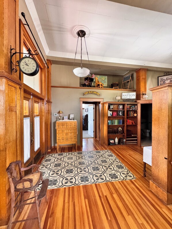 A wooden-floored hallway with a patterned rug, a clock, and a sign reading 'The Old Library.'