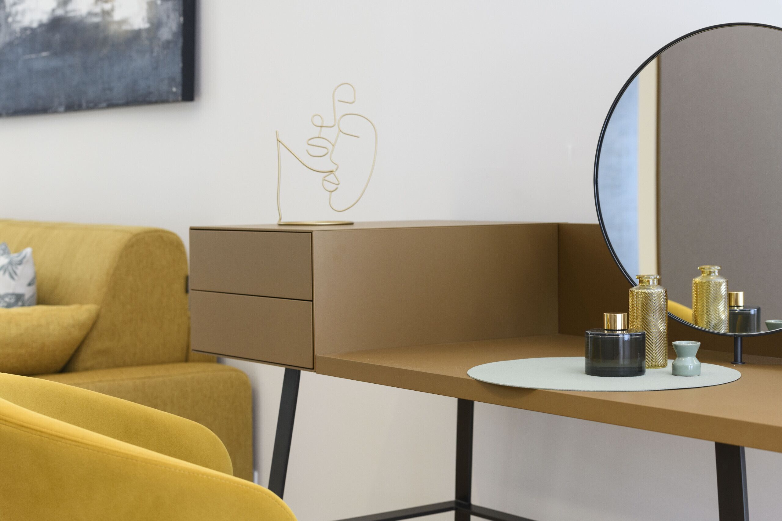 Ein modernes Zimmer mit einem gelben Sofa, einem Schreibtisch mit Spiegel und Dekorationselementen.