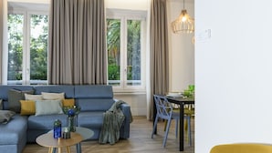 Een moderne woonkamer met een bank, een klein rond tafeltje, een eettafel met stoelen, en een raam met gordijnen.