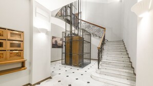 A staircase with a metal railing and a wooden handrail, leading to a landing with a white wall and a framed picture. - Domus Augustea - Cesare (Roma)