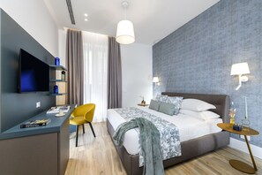 Ein modernes Hotelzimmer mit einem Bett, einem Schreibtisch mit Flachbildfernseher, einem gelben Sessel und zwei Nachttischen mit Lampen.